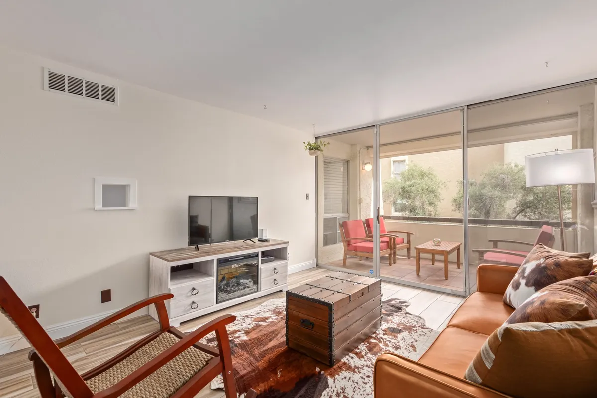 The image showcases a stylish and inviting living area with a comfortable seating arrangement around a sleek coffee table, a large flat-screen television, and expansive windows that bathe the room in natural light. The view from the windows hints at scenic sunsets, creating a serene atmosphere perfect for relaxation or entertaining. The space feels modern yet cozy, ideal for unwinding after a day exploring Scottsdale.
