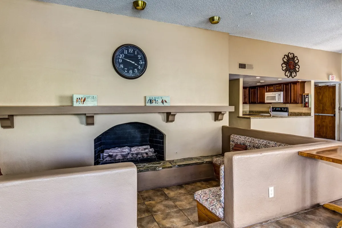 A warm, inviting interior featuring a cozy fireplace as the focal point, a classic wall clock above, and an open kitchen area in the background. The scene exudes a sense of comfort and hospitality, emphasizing the communal spaces available for relaxation after exploring the city.