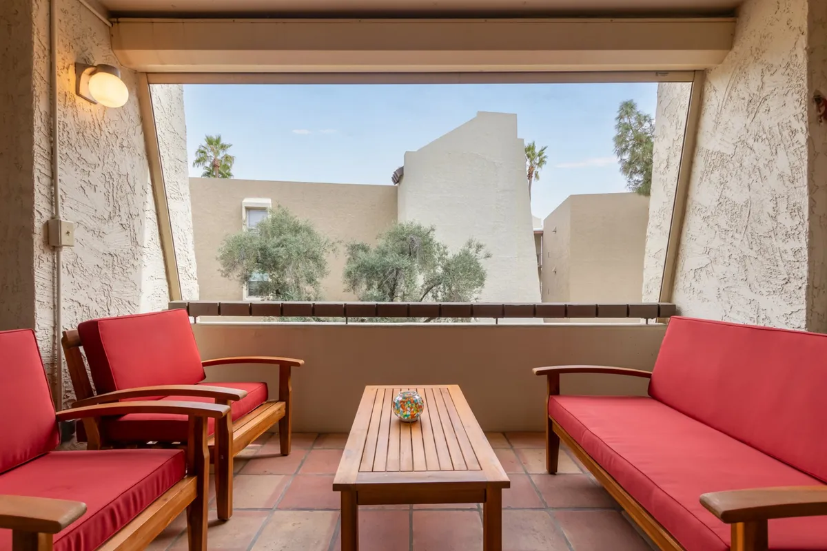 This image features a cozy living area with red seating, a wooden coffee table, and a window offering a view to the outside. The space is bathed in natural light, providing a tranquil spot for relaxation or casual conversation with a view of the neighborhood.