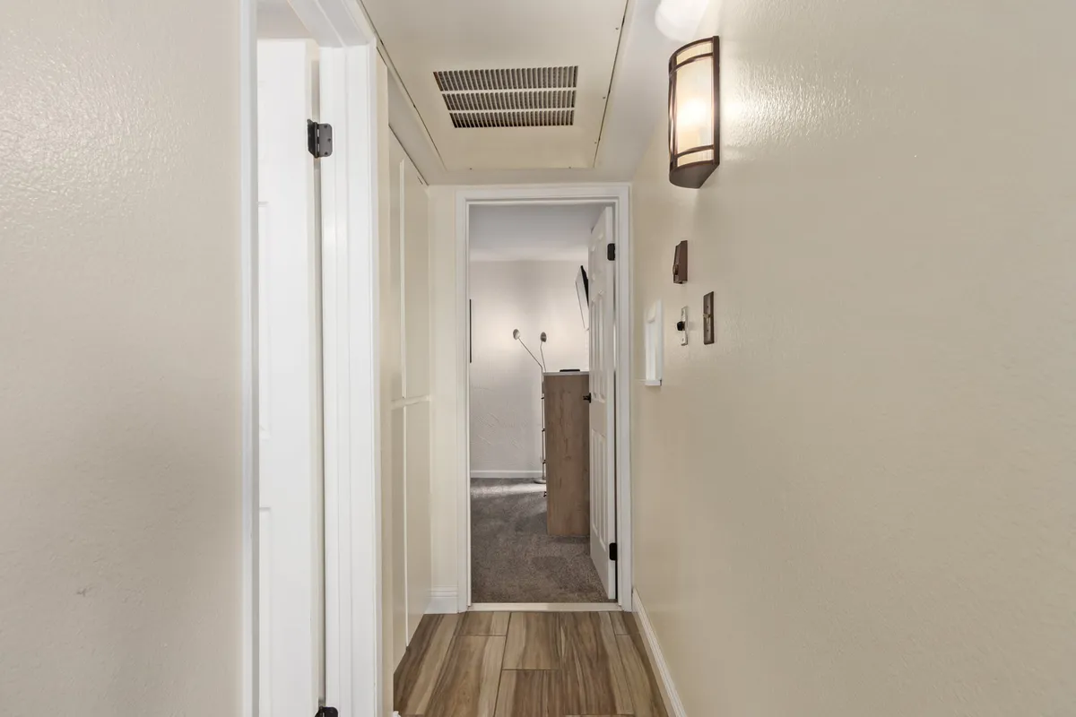 A hallway with a stylish light fixture, doors leading to other spaces, and attractive flooring. The perspective highlights movement through the home, suggesting the flow from the entrance to various communal and private areas.