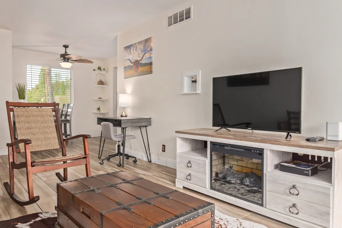 This indoor lounge area features a comfortable rocking chair, a wooden coffee table, a television, and eye-catching wall art. The space feels cozy and is ideal for relaxing, socializing, or enjoying a quiet moment indoors.