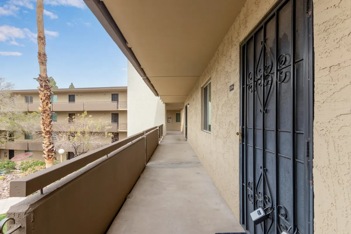 This image features a balcony view with a railing in the foreground, a door with a security gate, and a palm tree visible in the background. The angle highlights the sense of privacy while still providing an open-air feeling and a relaxing connection to the outdoors.