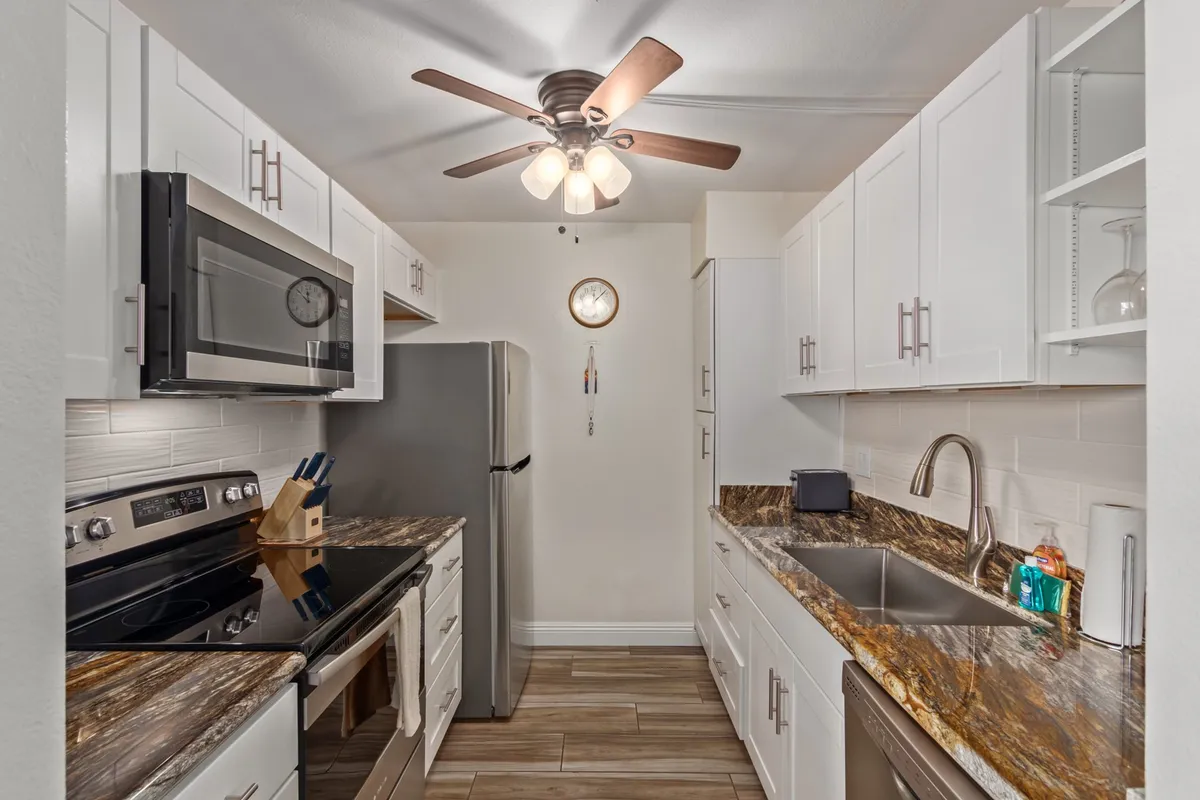A sleek, modern kitchen featuring granite countertops, stainless steel appliances, contemporary cabinetry, and a ceiling fan. The kitchen is bright and well-organized, offering a welcoming and functional space for meal preparation and entertaining.