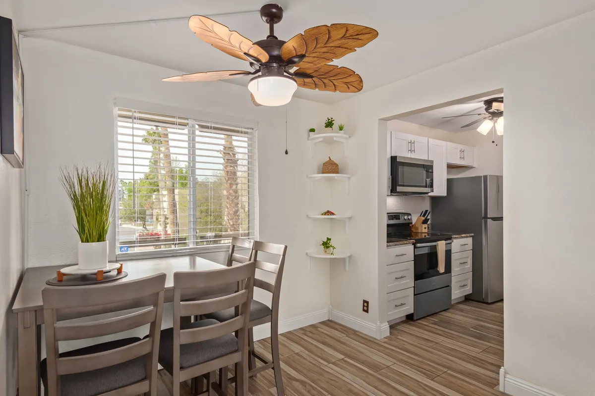 A bright dining area complete with a dining table, ceiling fan, and visible kitchen appliances and shelving. The space suggests mornings spent over coffee, casual meals, and a welcoming atmosphere ideal for both work and relaxation.